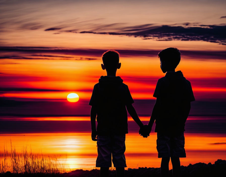 Silhouettes of two children holding hands at sunset with streaked clouds