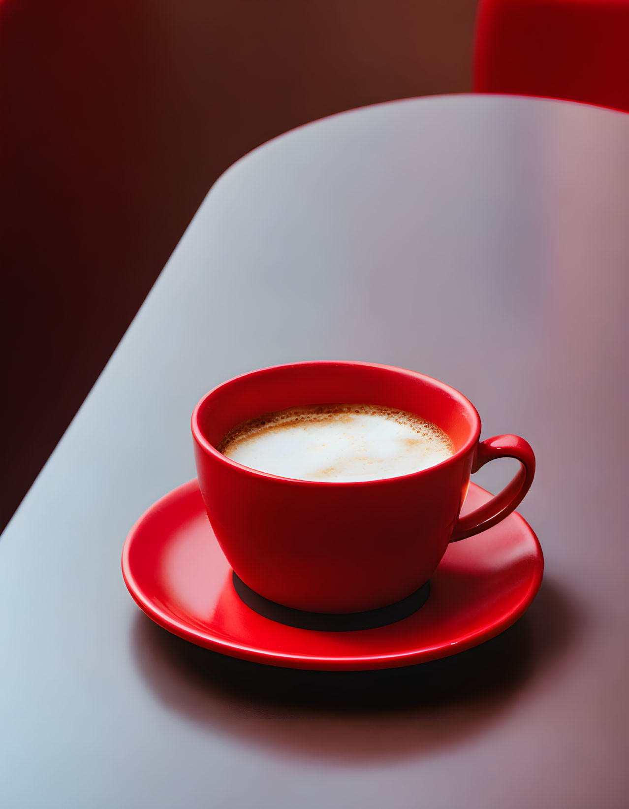 Red coffee cup with froth on saucer, on red table - softly lit background