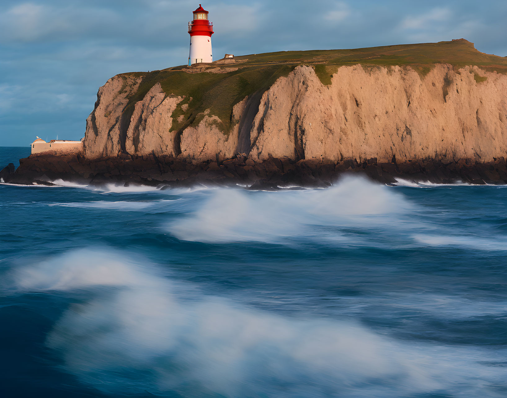 Red and White Lighthouse on Rugged Cliff with Crashing Waves