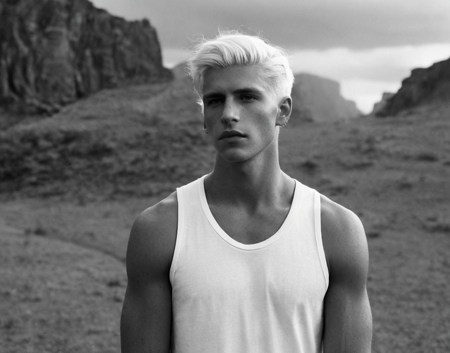 Monochrome portrait of man with platinum blonde hair against mountain backdrop