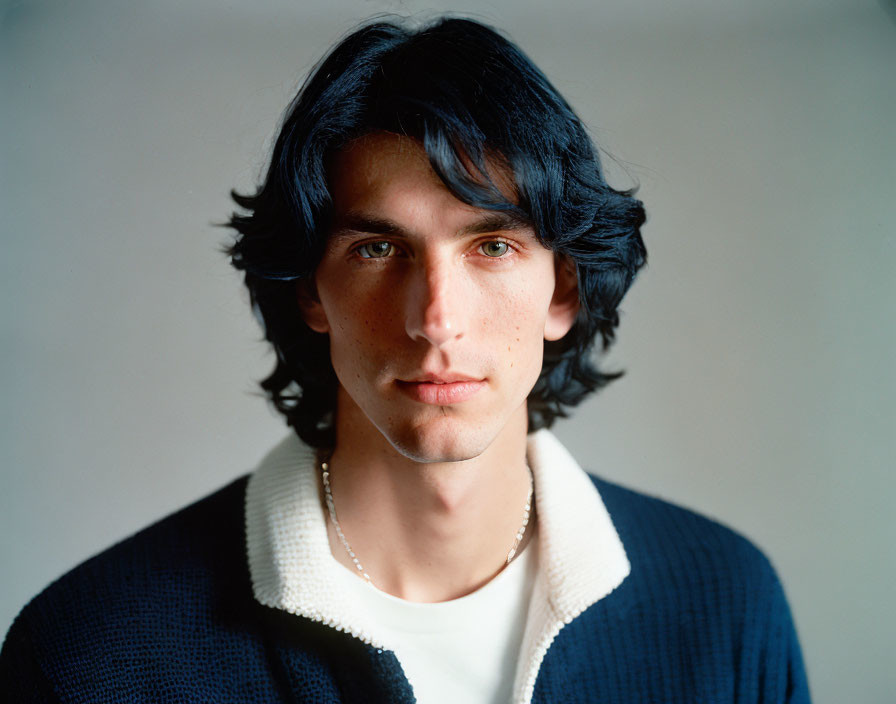 Young man with dark hair and blue eyes in blue and white sweater, neutral expression.