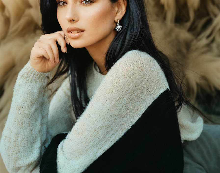 Dark-haired woman in white and black sweater with statement earrings poses against blurred natural backdrop