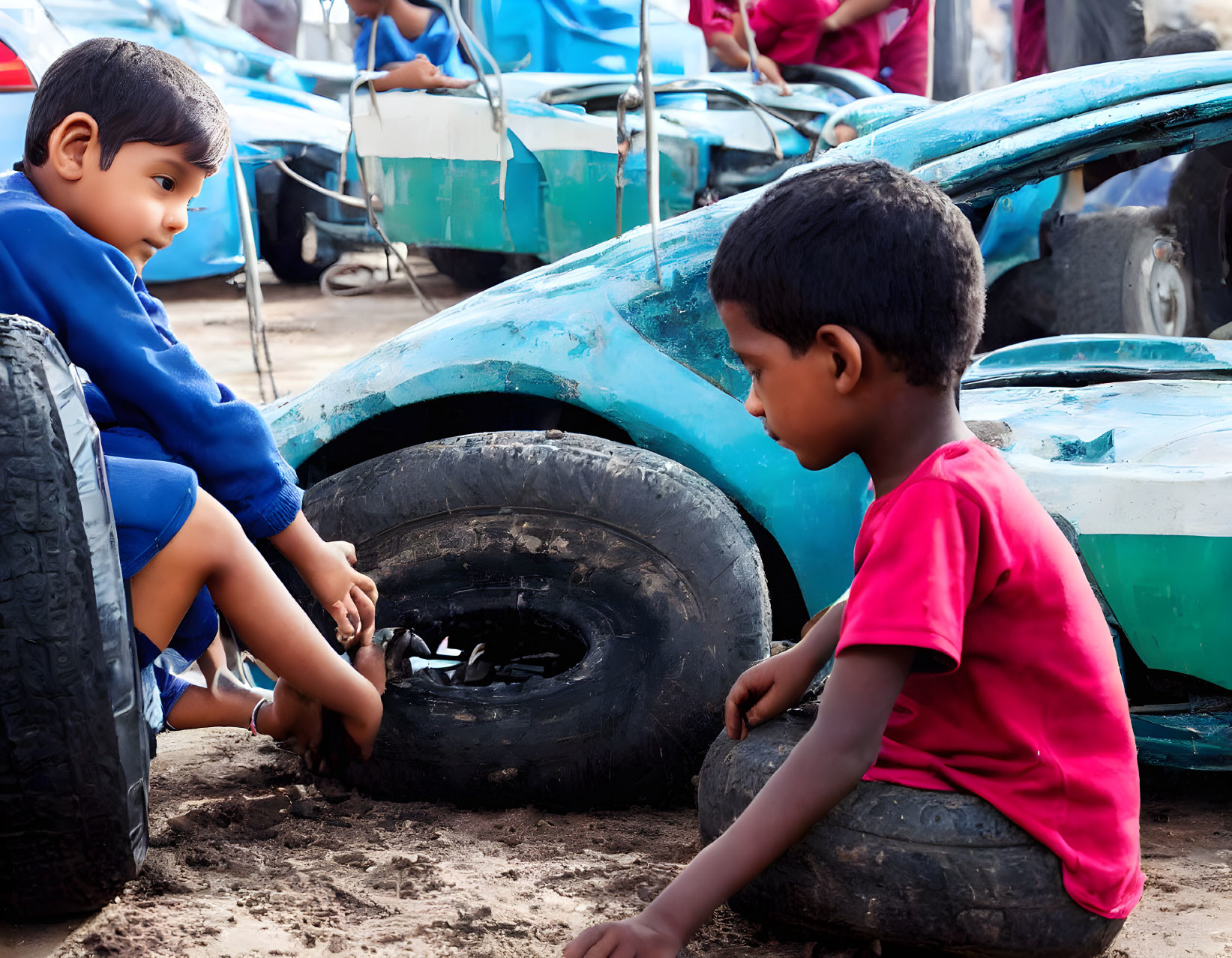 Children playing with tire and toy car on sandy ground.