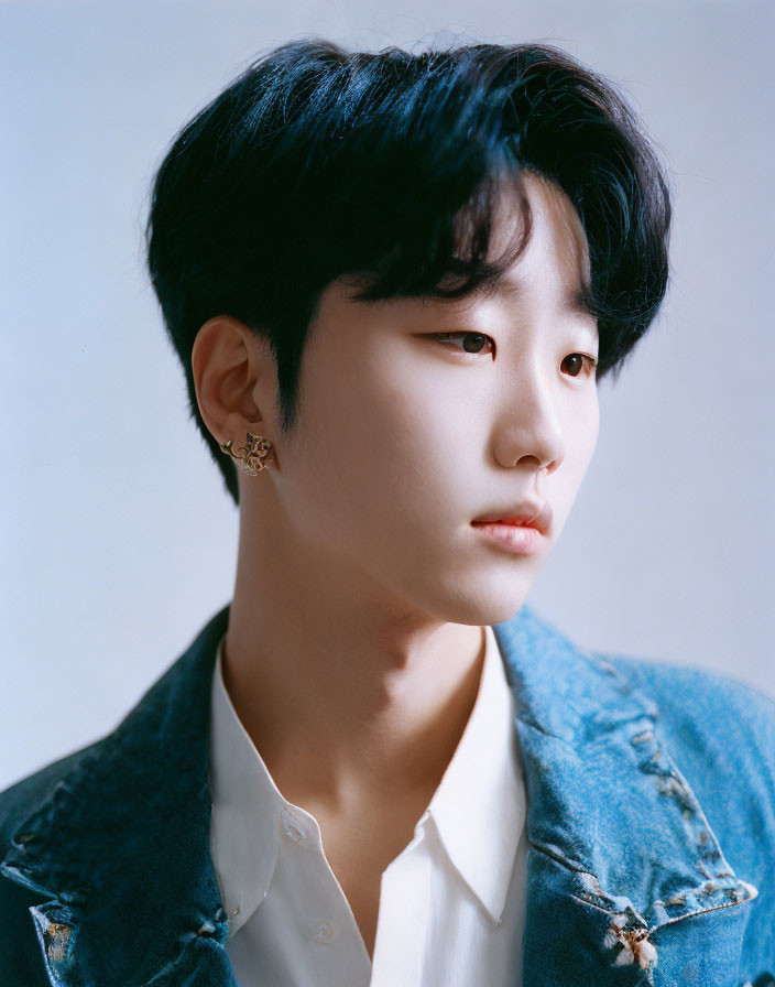 Young person in denim jacket and white shirt with dark hair, looking sideways.