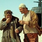 Elderly gentlemen in steampunk attire with brass telescope and flying machine in desert.