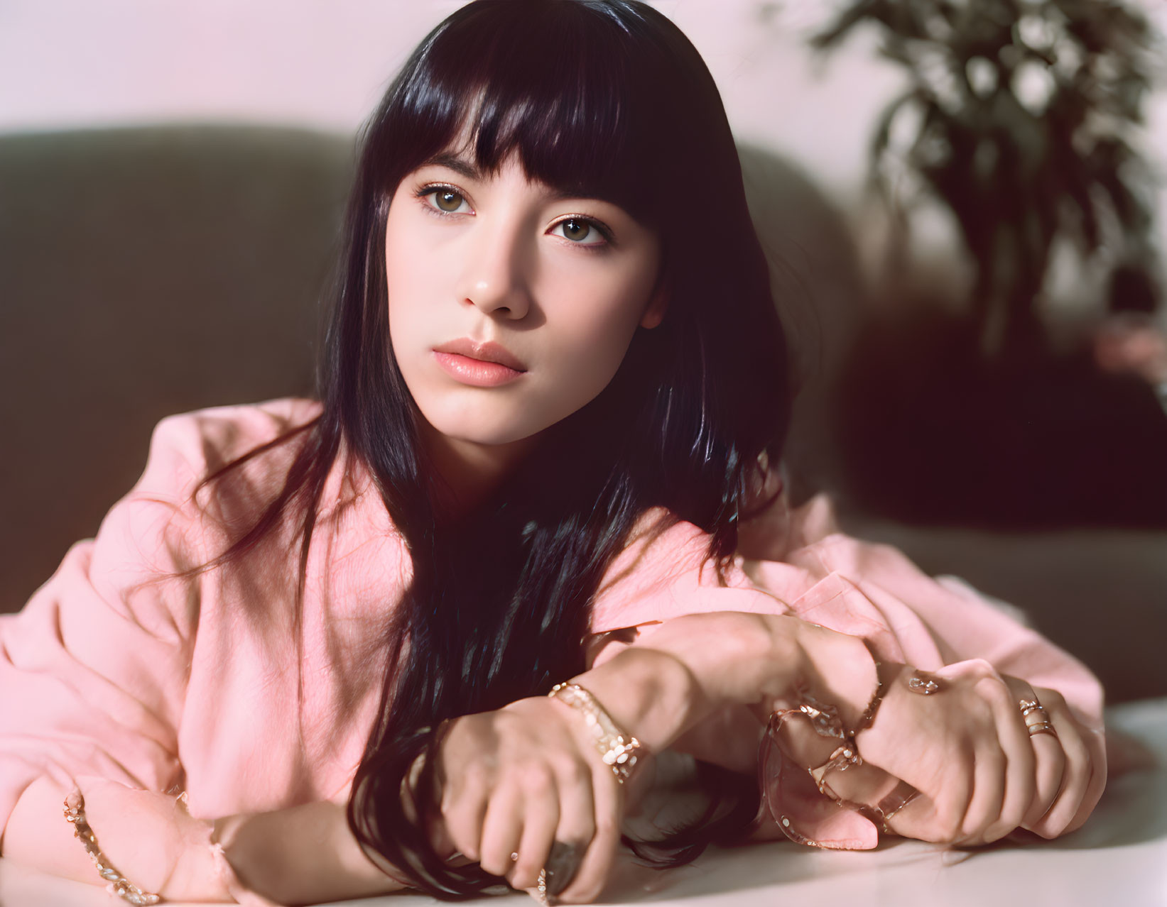 Long-haired woman in pink attire with gold bracelets, posing for the camera