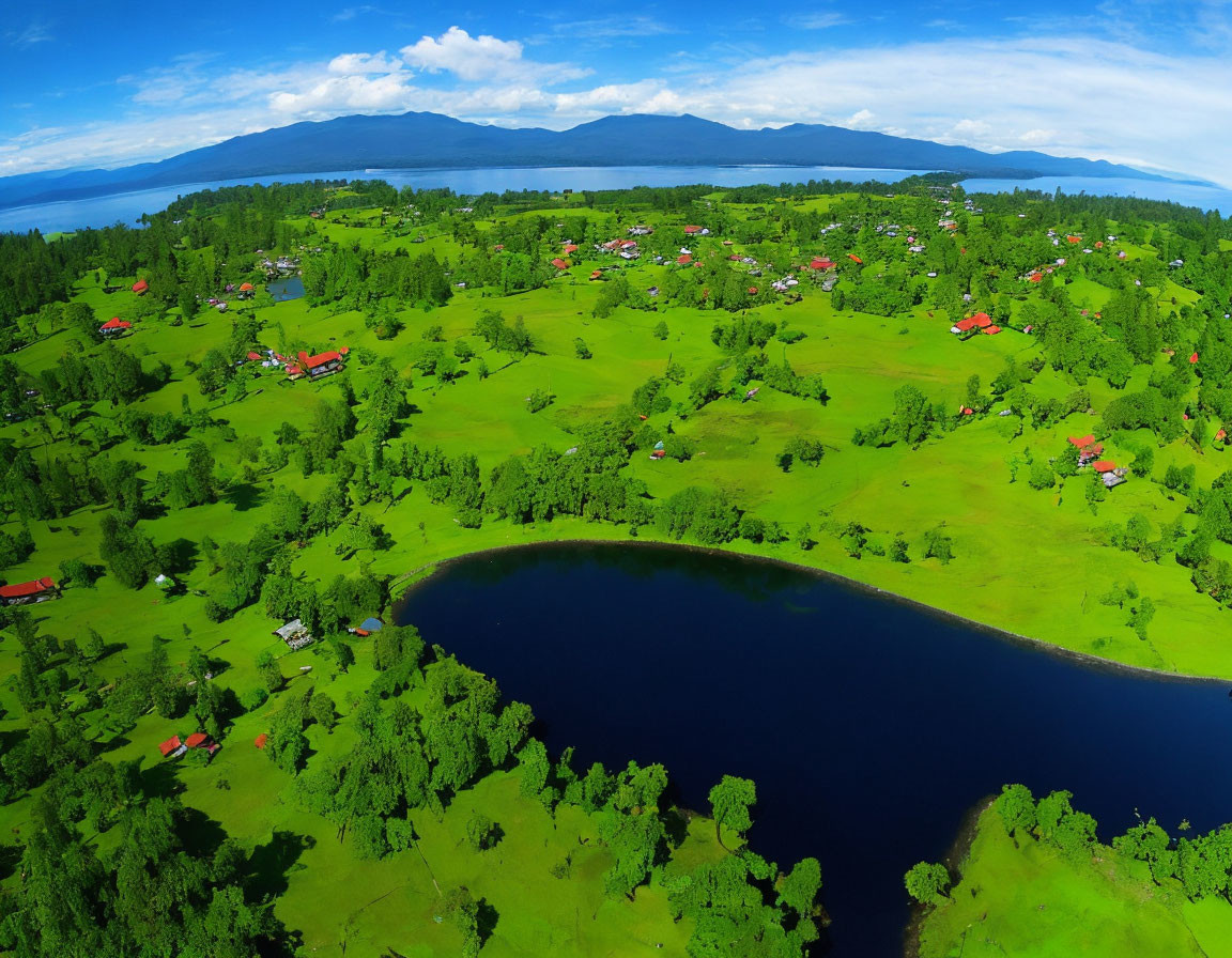 Scenic aerial view of lush green landscape with village, lake, trees, and mountains