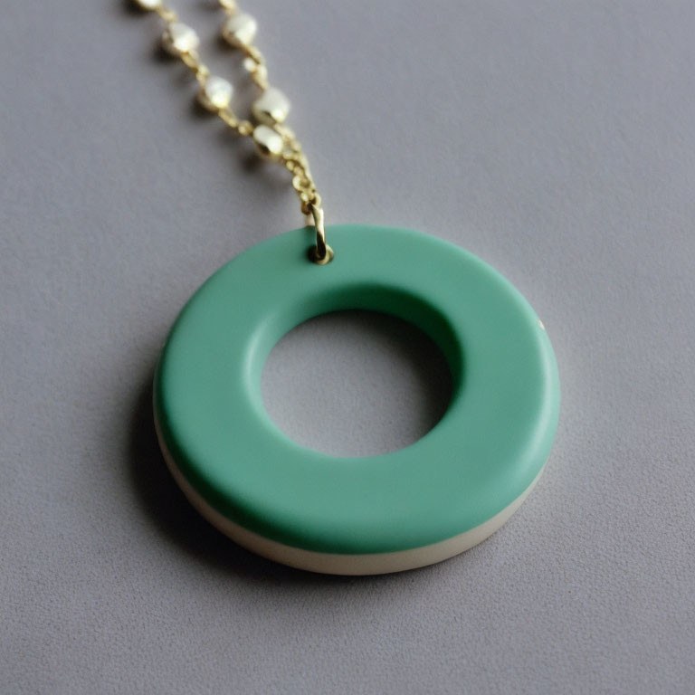 Mint Green and White Circular Pendant on Gold Chain on Grey Background