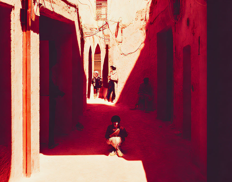 Child in shadowy alley with red walls and passersby.