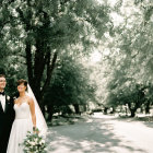 Bride and groom holding hands beneath tree canopy on sunlit road