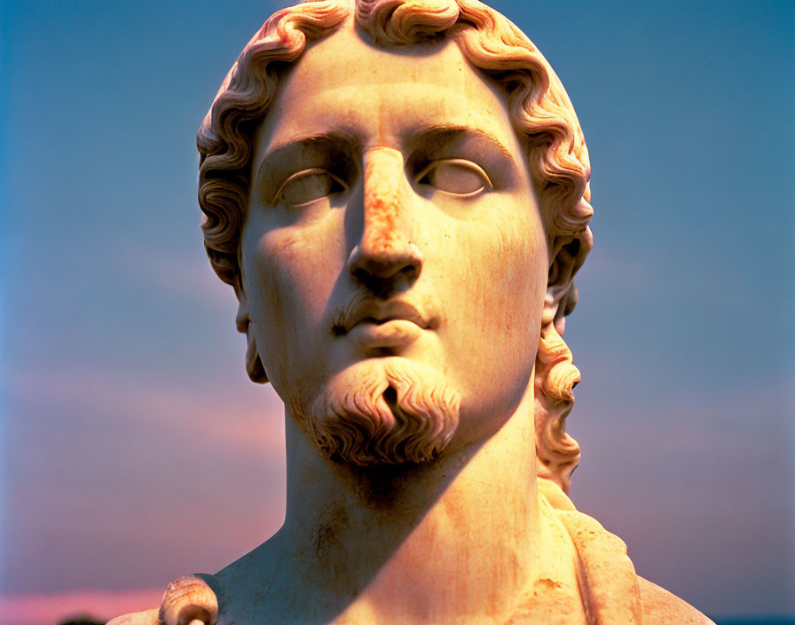 Classical sculpture of male figure with curly hair and serene expression under twilight sky