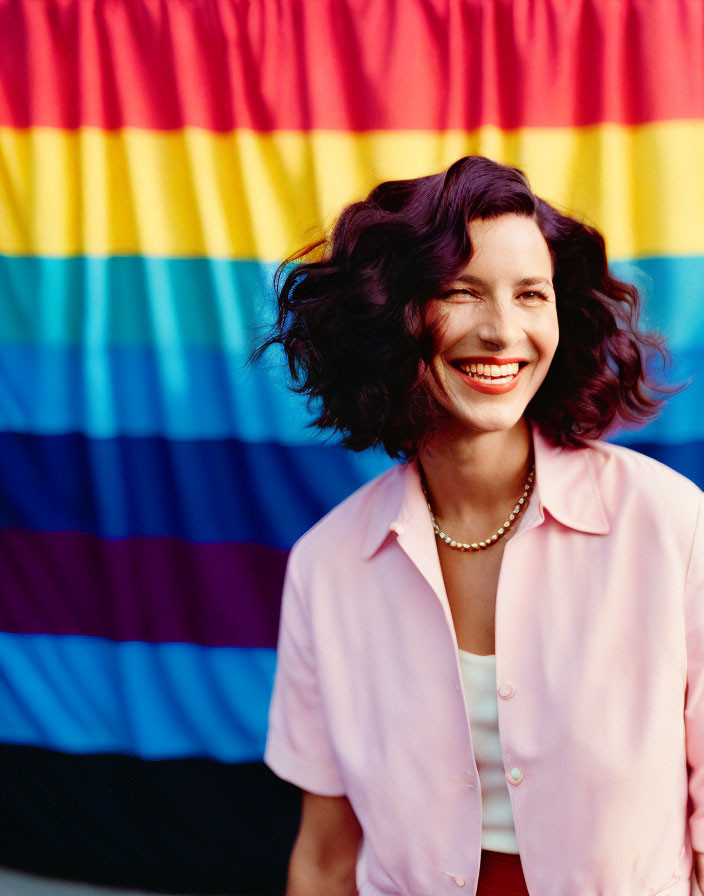 Smiling woman with short curly hair in pink shirt against colorful striped background