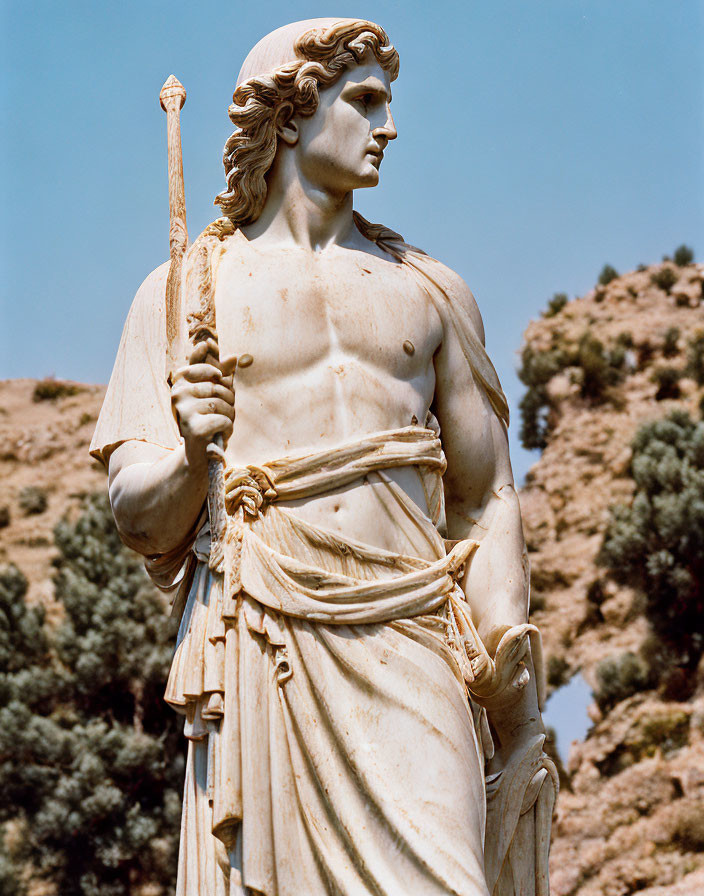 Muscular male figure statue with spear, draped cloth, against sky and greenery