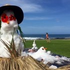 Snowman with ukulele, small snowman, and maracas on sunny beach with people and