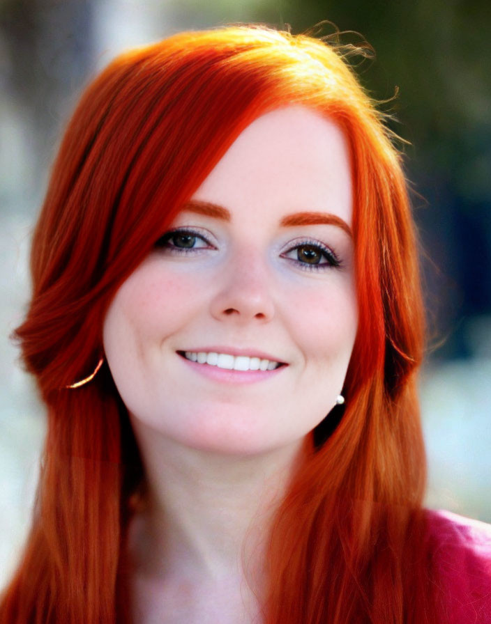 Smiling woman with red hair and blue eyes in red top and hoop earrings