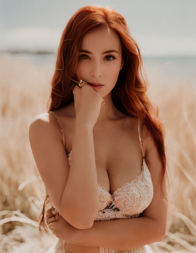 Red-haired woman in lace top posing in sunlit field