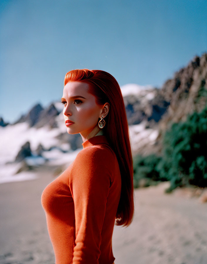 Red-haired woman in orange top against snowy mountain backdrop