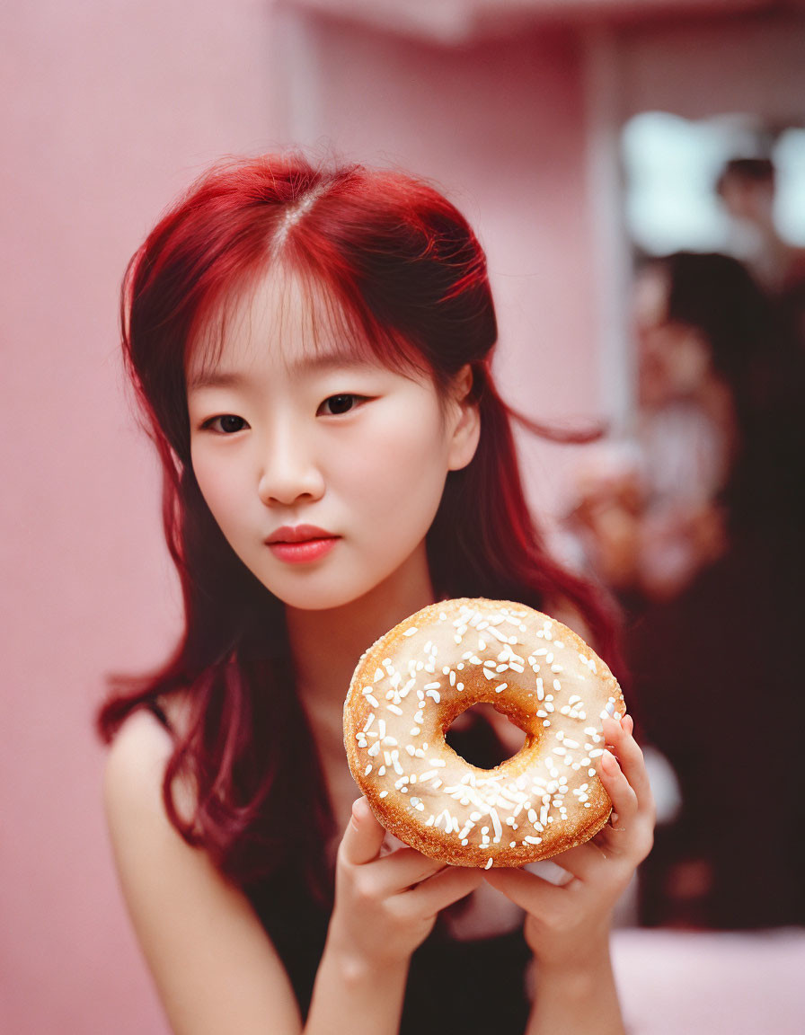 Red-haired woman holding frosted donut on pink background