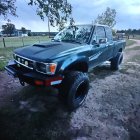 Custom blue off-road truck with large spoiler and roof lights on rocky terrain