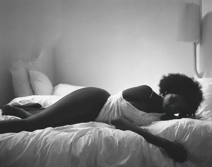 Monochrome photograph of woman resting on bed in dimly lit room