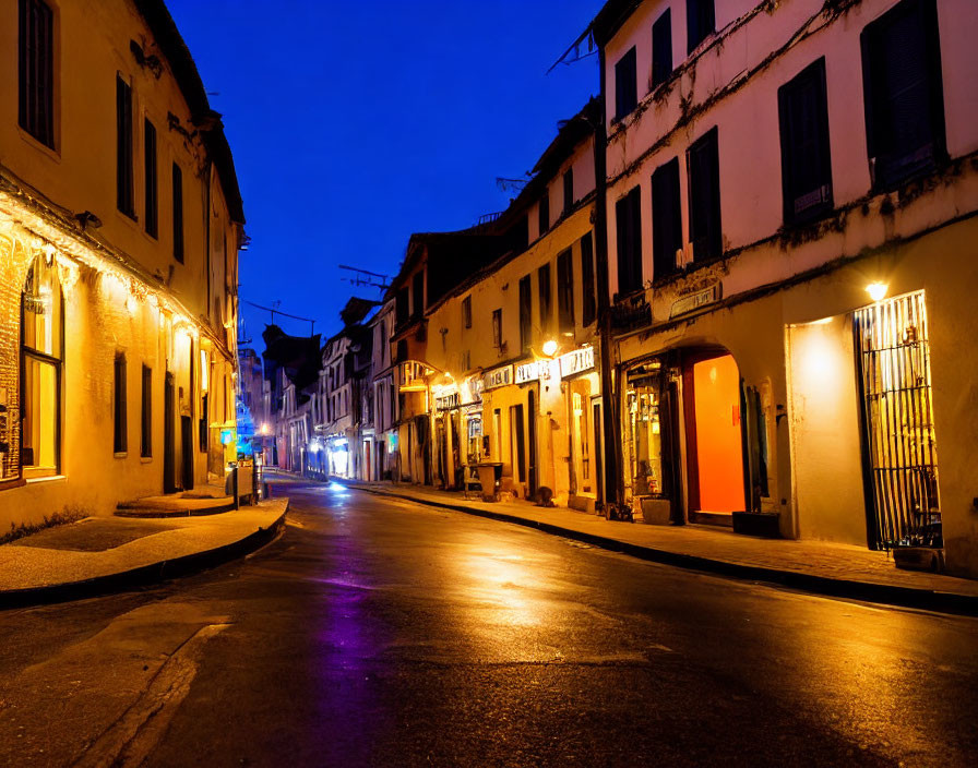 Twilight streetscape with illuminated shopfronts and wet street reflections