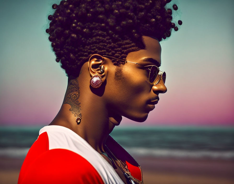 Profile view of stylish person with afro, sunglasses, and earrings at sunset beach