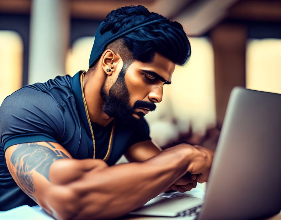 Bearded man with headband working on laptop with tattooed arms