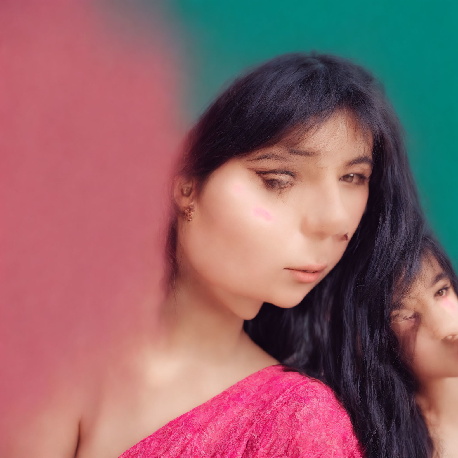 Dark-haired woman with pink blush mark, teal background, and out-of-focus person.