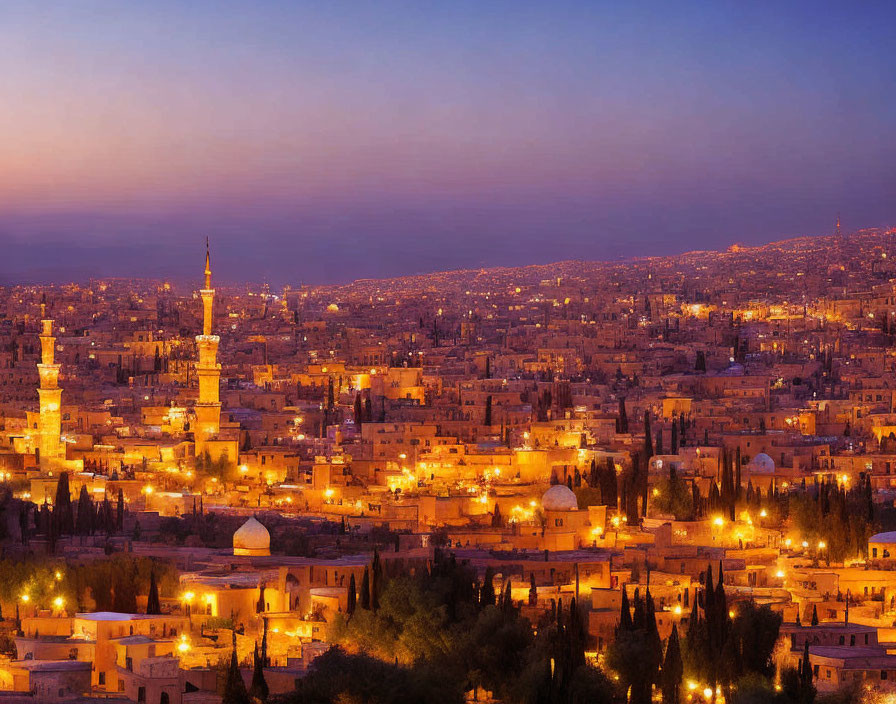 Cityscape panorama: twilight view with illuminated buildings and minarets under a warm evening sky.