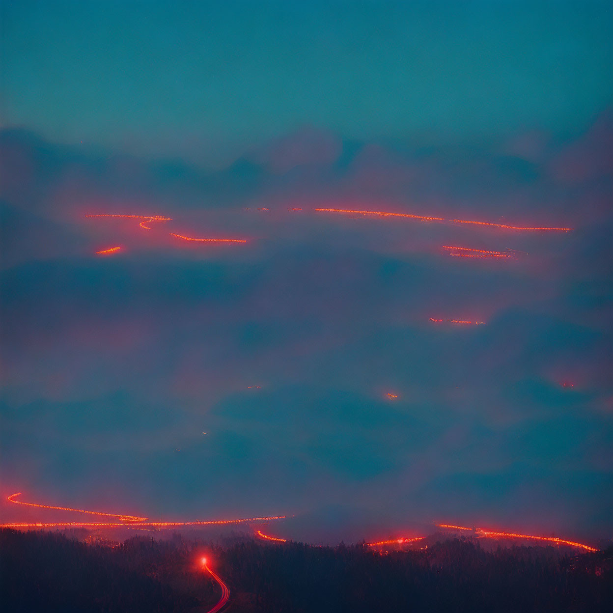 Twilight long exposure of winding mountain roads with glowing red light trails