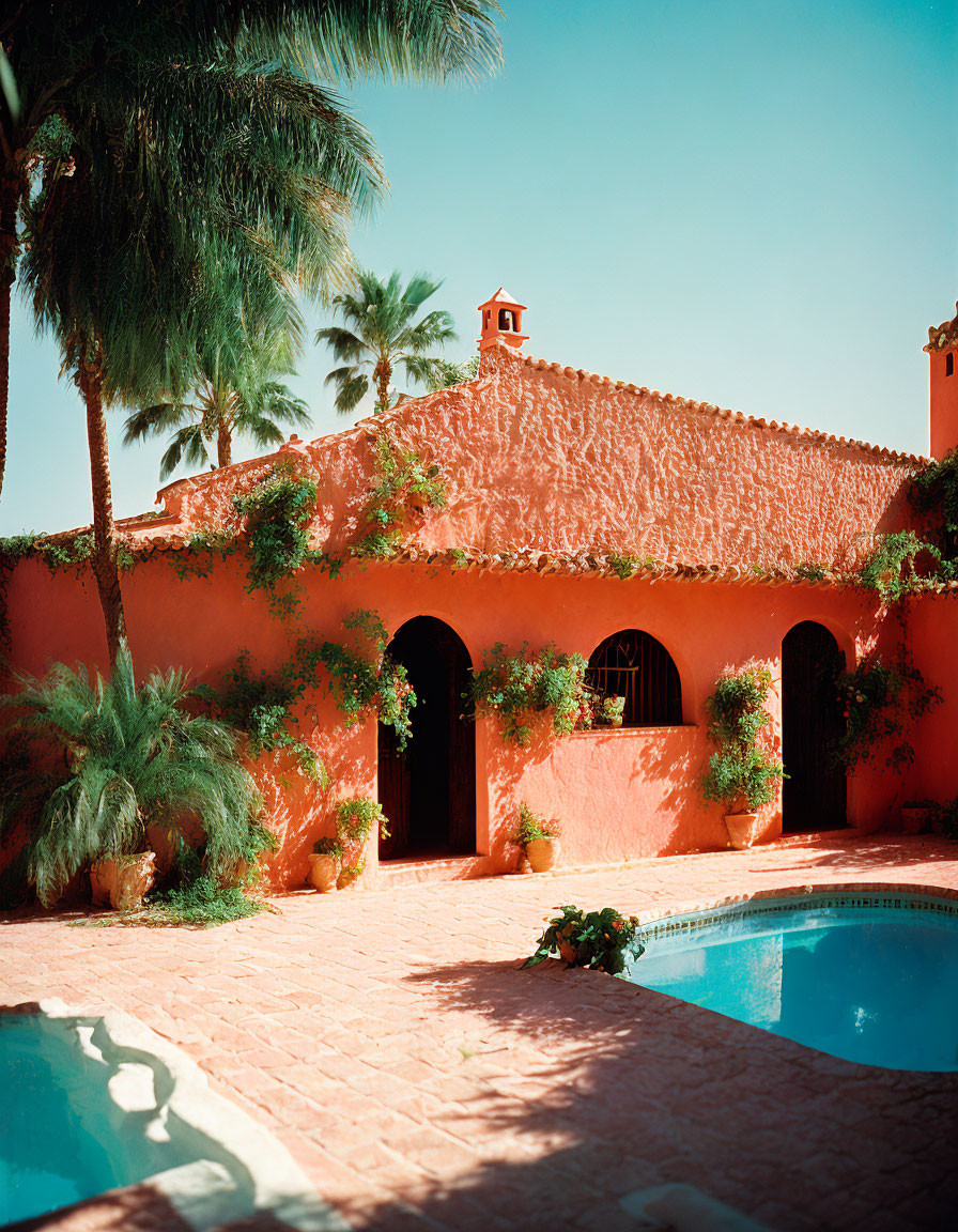 Terracotta-colored villa with archways, swimming pool, tropical palms, clear sky