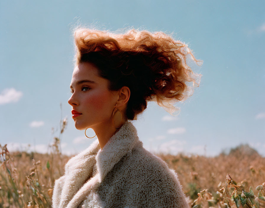 Woman in cream coat with windblown hair under blue sky