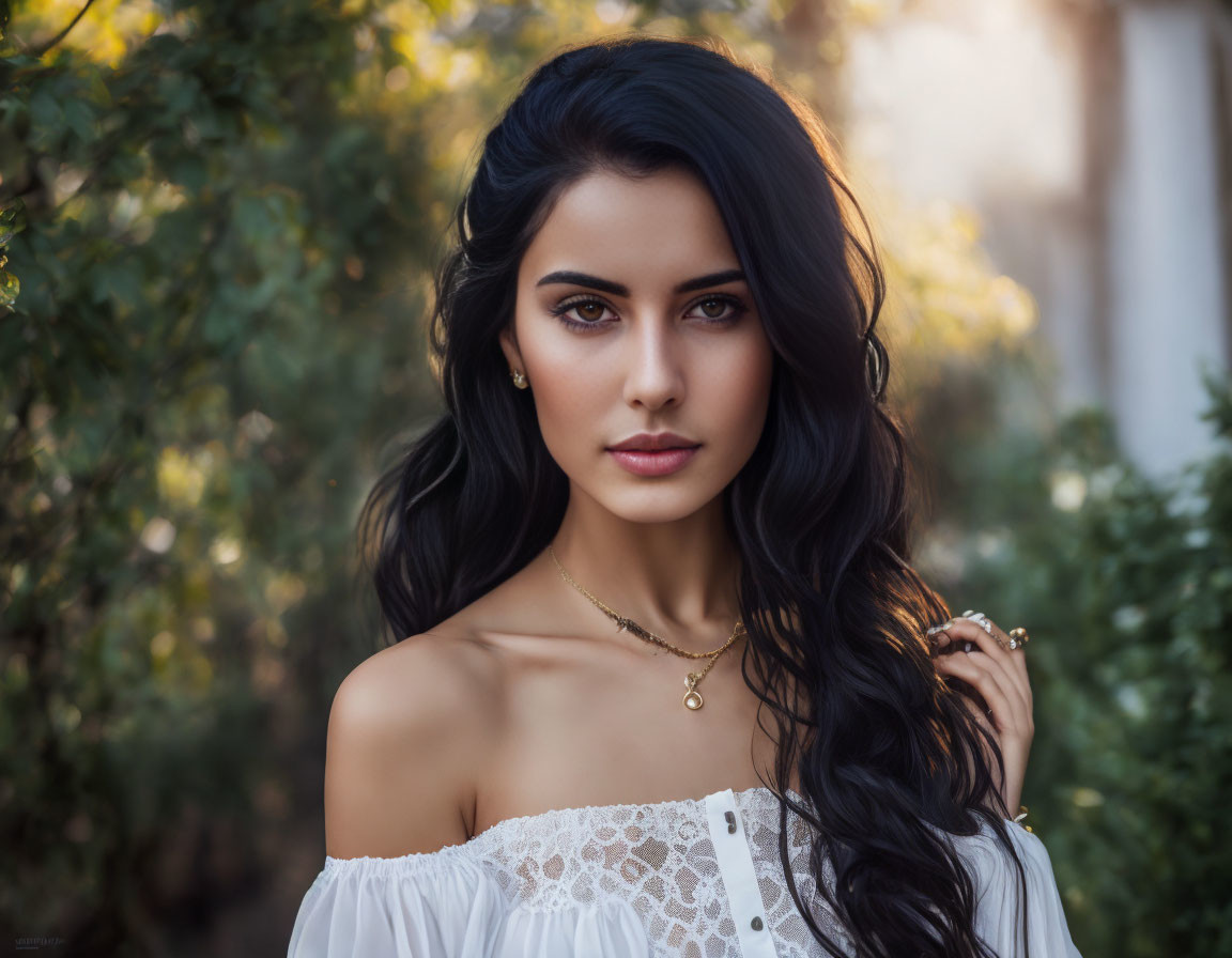 Woman with long dark hair and blue eyes in white off-shoulder top among green foliage