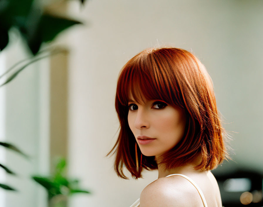 Red-haired woman with shoulder-length hair and bangs in indoor setting.