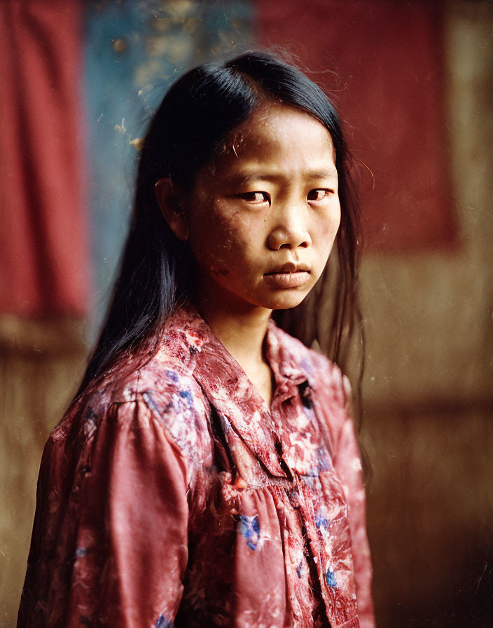 Portrait of young girl with long black hair in red floral shirt against red and blue backdrop