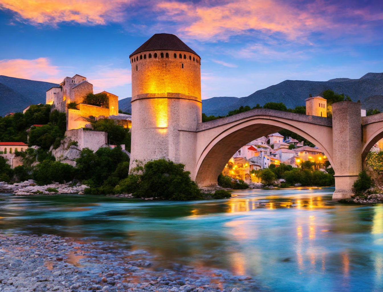 Historic stone bridge with tower over tranquil river at sunset