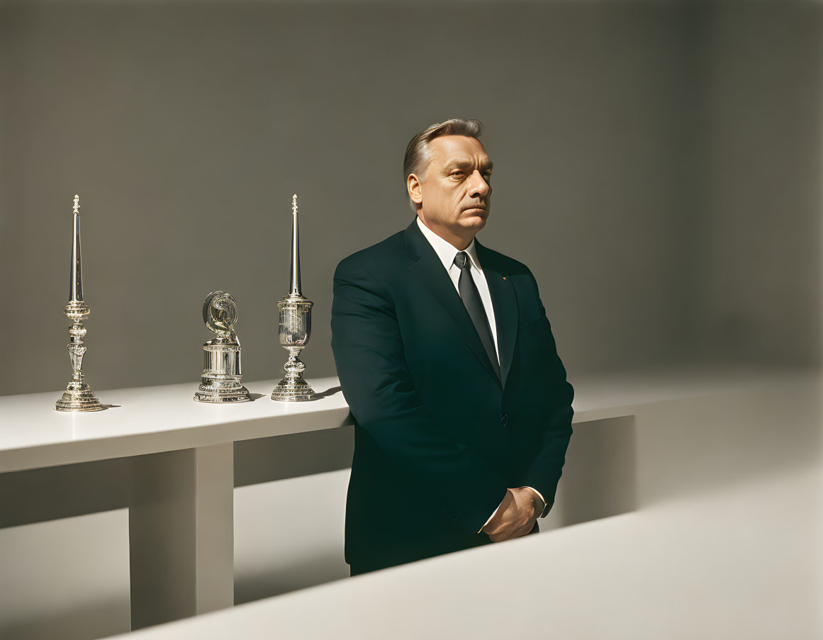 Man in suit by table with silver trophies under spotlight