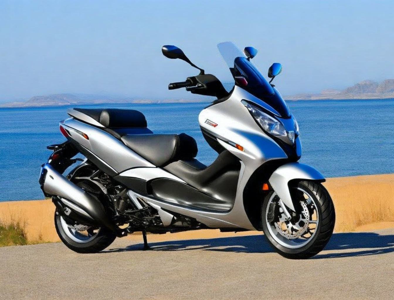 Silver modern scooter on sandy beach with clear blue skies and calm sea