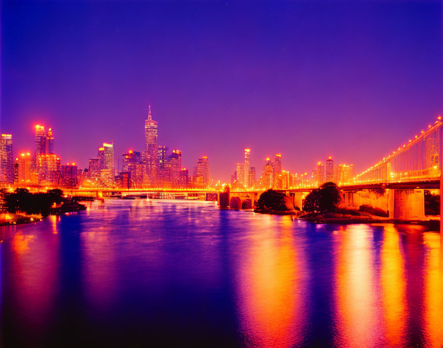 Twilight cityscape with illuminated high-rises and lit bridge over tranquil river under purple sky