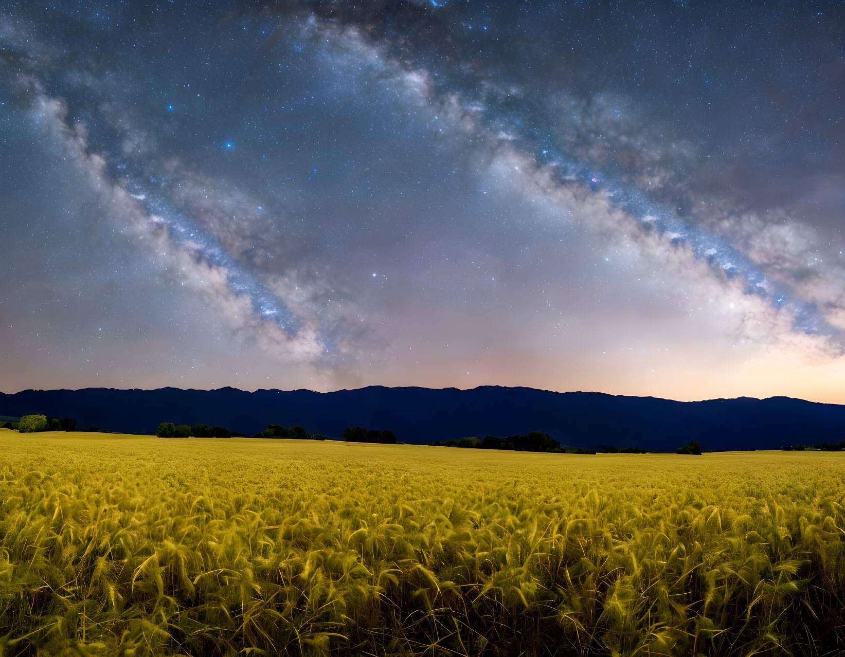 Panoramic night sky over golden wheat field and mountains