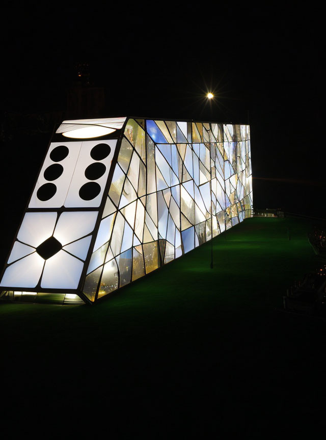 Modern glass building resembling giant domino at night with illuminated windows