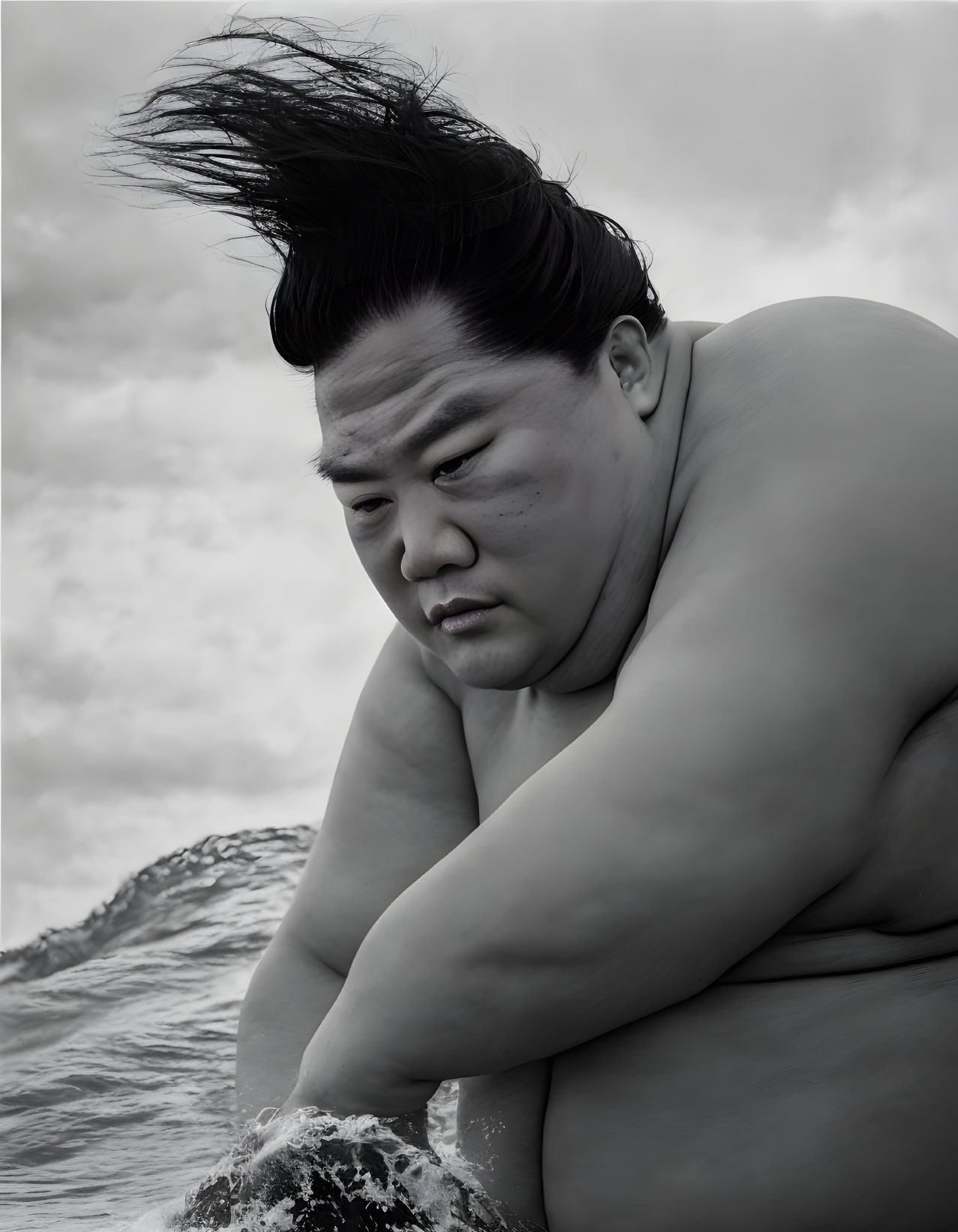 Monochrome image: Sumo wrestler by water, deep in thought