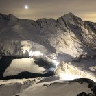 Majestic mountain peaks, village on bridges, serene lake at dusk