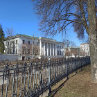 Classical building with wrought-iron fence, trees, purple flowers, blue sky