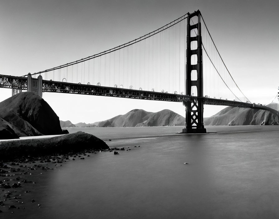 Monochrome image of Golden Gate Bridge over serene bay with hills.