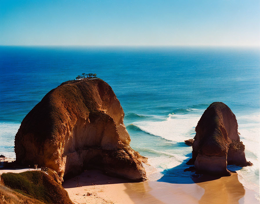 Coastal view with large rock formations, crashing waves, and clear sky