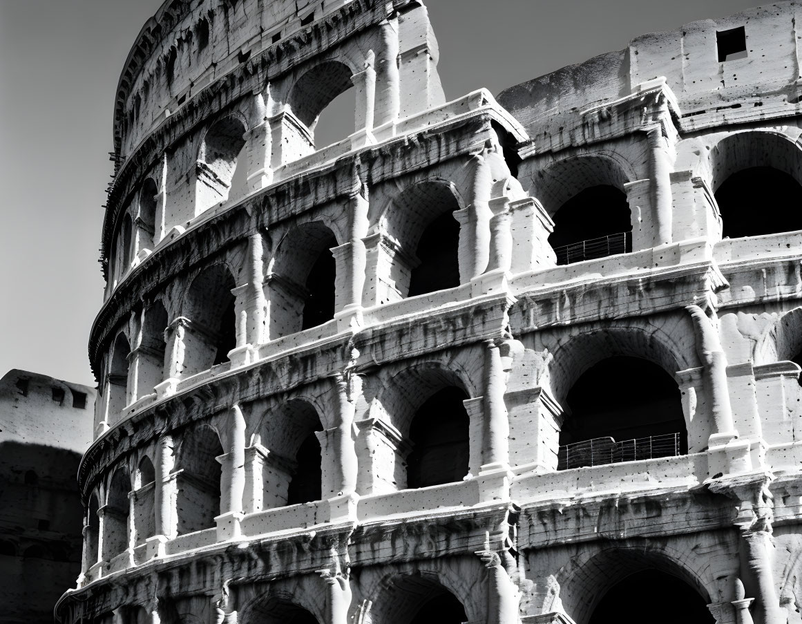 Monochrome image of aged Colosseum arches and ruins against bright sky