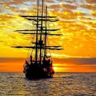 Sailboat with lowered sails against sunset over calm seas