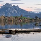 Tranquil lake scene with wooden pier, pine trees, and snow-capped mountains