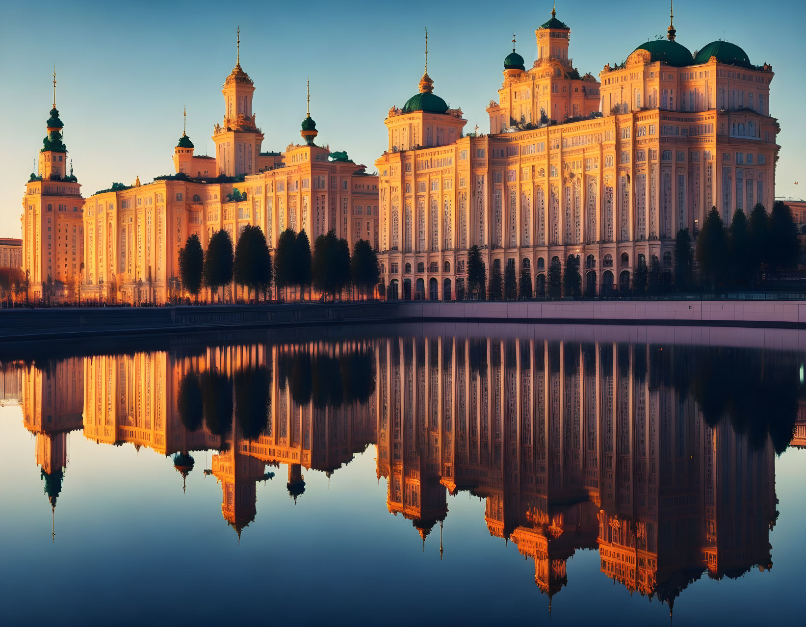 Majestic building with green domes by calm water at twilight